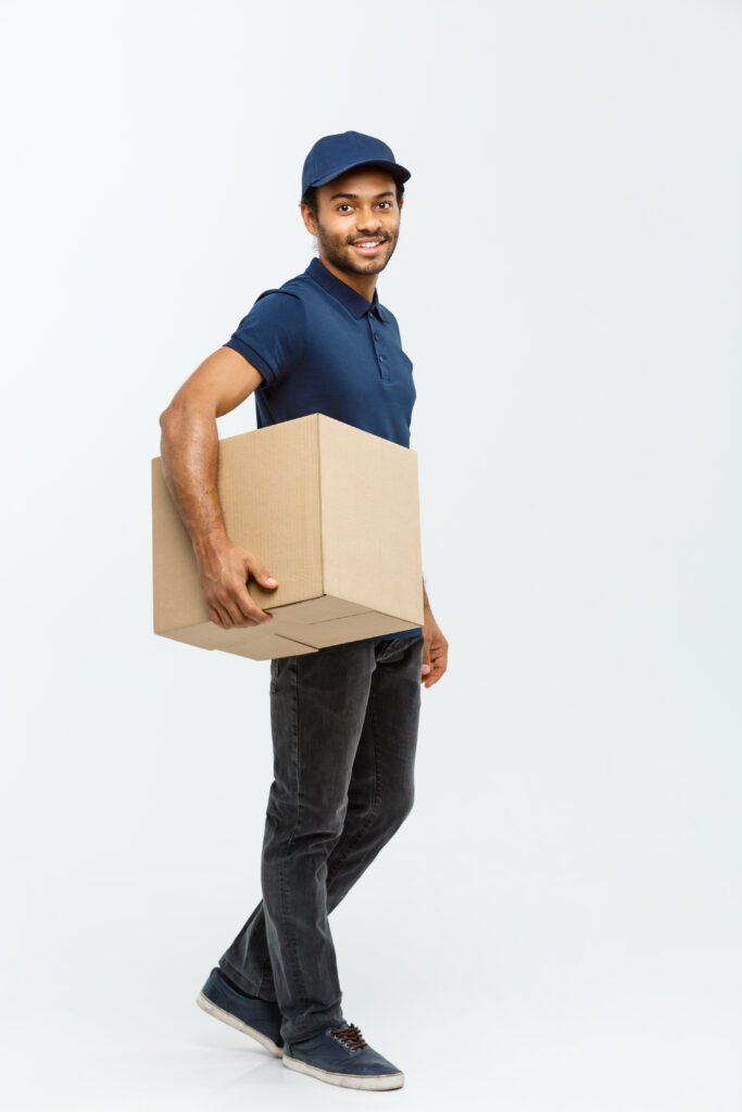 delivery concept portrait of happy african american delivery man in blue cloth walking to send a box package to customer. isolated on grey studio background. copy space. delivery concept portrait of happy african american delivery man in blue cloth walking to send a box package to customer. isolated on grey studio background. copy space.